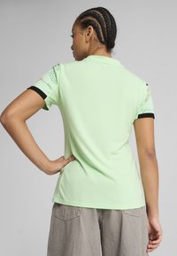 Polo vert clair avec des bordures noires sur les manches, présentant des accents texturés à motifs aux épaules et une texture de corps lisse.