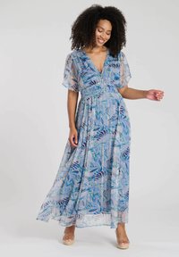 Robe maxi en tissu bleu clair avec des motifs de feuillage dans des bleus et verts plus foncés, manches courtes et décolleté en V. Design fluide.