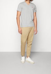 Graues V-Ausschnitt-T-Shirt mit kurzen Ärmeln, kombiniert mit beigen Chinos und weißen Sneakern. Einfaches Design, weiche Textur, minimales Branding.