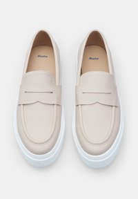 Beige ādas loafers ar priekšējo siksniņu, apaļu purngalu un baltu gumijas zoli. Iekšējā zole ir nedaudz polsterēta komfortam.