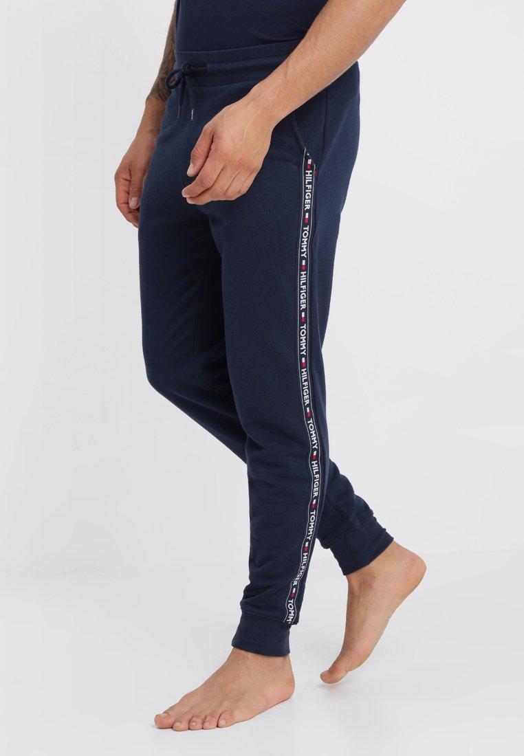 Granatowe dresy w zwężanym fasonie, z kontrastowymi paskami po bokach z brandingiem "Tommy Hilfiger" oraz w pasie na sznurek.