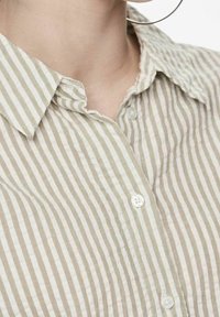 Striped button-up shirt in beige and light brown. Soft, textured fabric with a classic collar and visible button details.