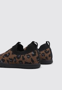Zapatillas slip-on con estampado de leopardo en marrón y negro, parte superior de punto, suela de goma negra y collar elástico para un fácil uso.