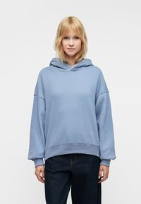 Felpa blu chiaro con vestibilità ampia, cappuccio regolabile con cordino e polsini a coste. Abbinata a jeans in denim scuro, dal design semplice.