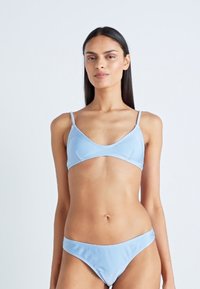 Šviesiai mėlynas bikinis, kuriame yra trikampė liemenėlė su plonomis petnešėlėmis ir atitinkamos žemos juosmens kelnaitės. Medžiaga yra lygi.