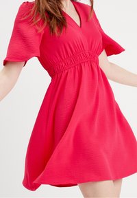 Robe rose à manches courtes avec un décolleté en V plongeant, tissu texturé, taille élastique et jupe évasée. Design simple et fluide.