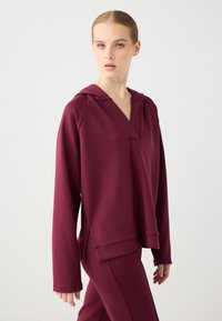 Bordowy hoodie z kapturem z miękkiego materiału, z dekoltem w serek, długimi rękawami i bocznymi rozcięciami, w komplecie z pasującymi spodniami.