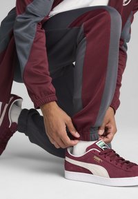Maroons- og grå træningstøj med elastiske manchetter, detaljeret syning, sammen med maroon Puma ruskinds-sneakers med hvidt logo og sål.