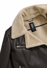 Bruine leren jas met een crème faux fur kraag, een diagonale ritszak en een stoffen label op de nek. Gladde textuur, gestructureerd ontwerp.