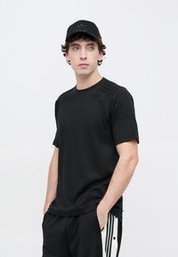 Μαύρο κοντομάνικο T-shirt από απαλό ύφασμα, με υφασμάτινες λεπτομέρειες στους ώμους. Συνδυάζεται με μαύρο παντελόνι και μαύρο καπέλο με λογότυπο.