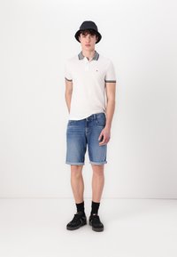 Hvit polo skjorte med grå detaljer, denimshorts, svart bøttehatt, svarte sokker og joggesko med kanvas tekstur og oppbrettede ermer.