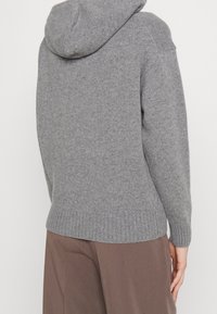 Szary sweter z dzianiny z kapturem, z prążkowanymi mankietami i dołem. Miękka tekstura, lekko luźny krój, minimalne detale szwów.