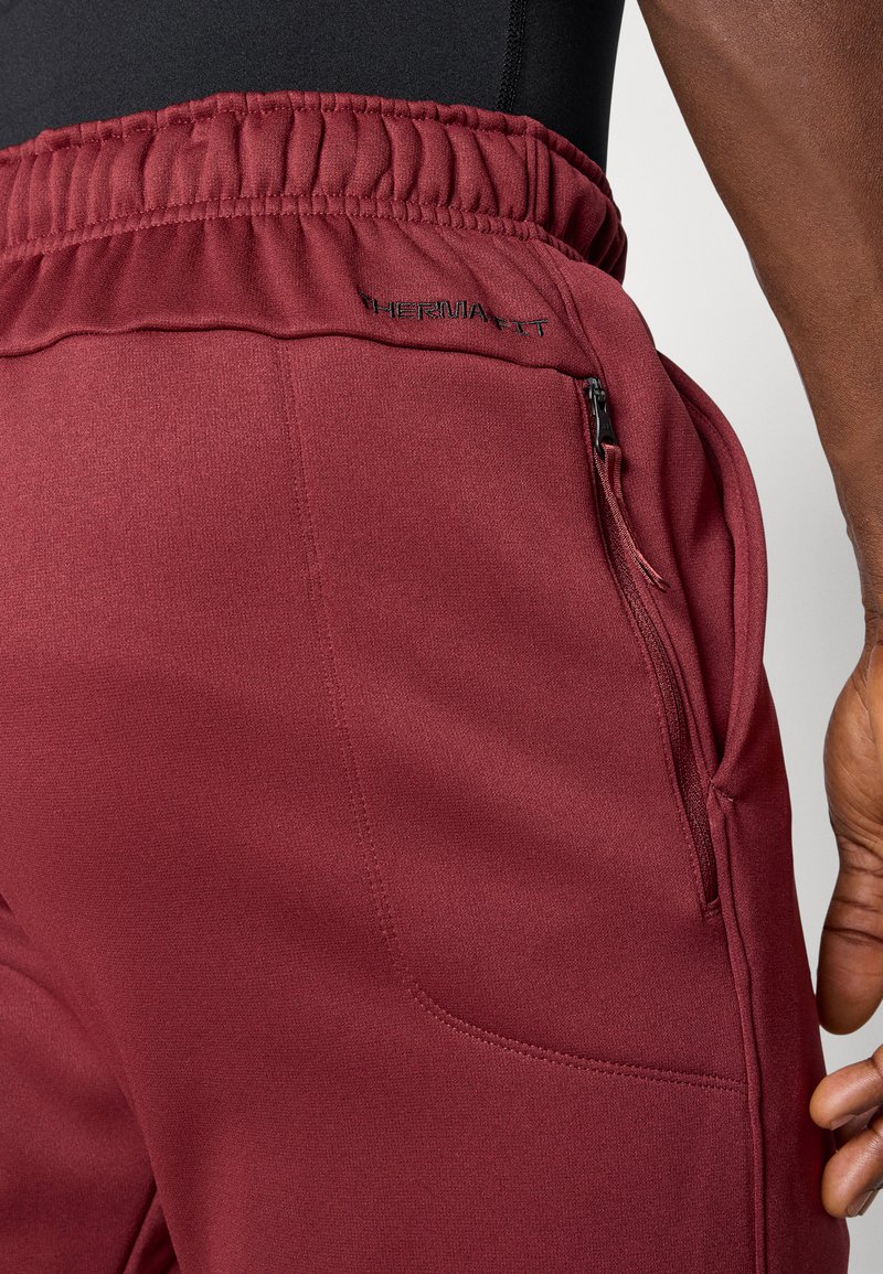 Pantaloni sportivi bordeaux con finitura testurizzata, dotati di una vita elasticizzata, tasca laterale con zip e branding THERMA FIT.