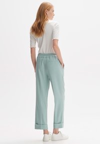 Pantaloni verde menta chiaro con una vestibilità rilassata, caratterizzati da una vita con cordoncino, tasche laterali e orli arrotolati. Abbinati a sneaker bianche.