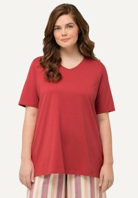 Volné červené tričko s výstřihem do V vyrobené z měkké látky, s krátkým rukávem a uvolněným střihem v kombinaci s pruhovanými kalhotami.