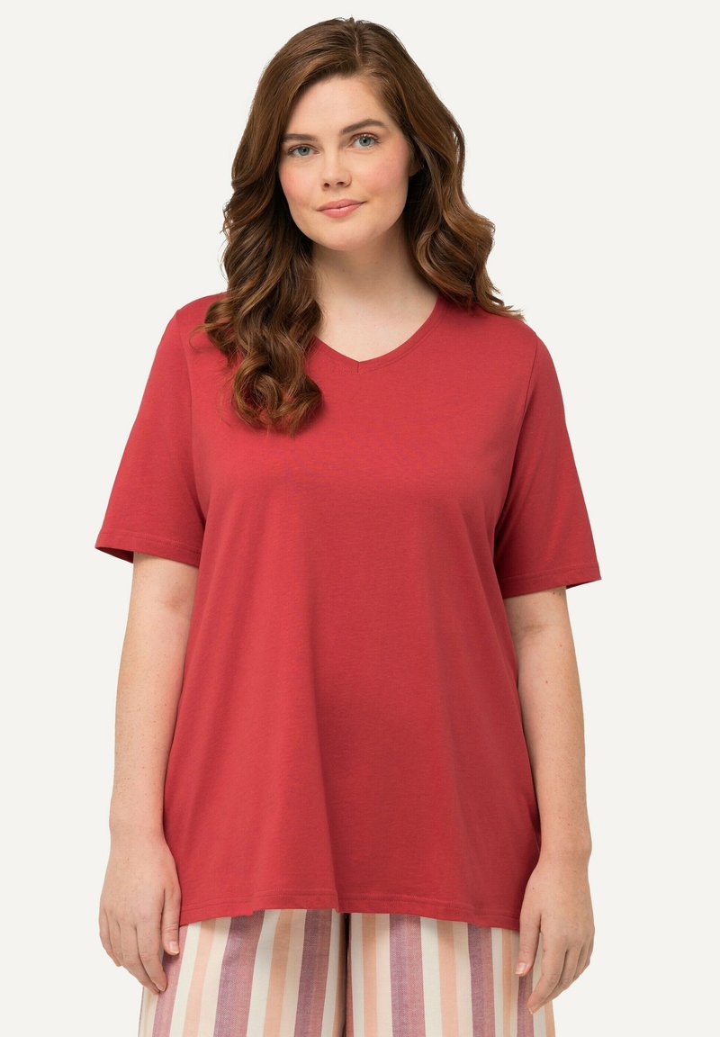 Volné červené tričko s výstřihem do V vyrobené z měkké látky, s krátkým rukávem a uvolněným střihem v kombinaci s pruhovanými kalhotami.