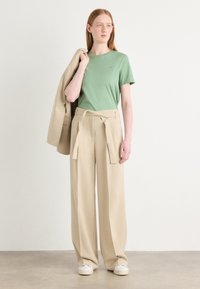 T-shirt in cotone verde, pantaloni larghi beige a vita alta con cintura legata e sneaker bianche. Design semplice, texture liscia.