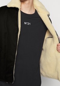 Czarna kurtka rozpinana z kremowym futrem, noszona na ciemnym t-shircie z napisem "N°21" w białym kolorze.