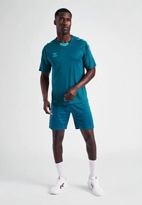 Camiseta deportiva y pantalones cortos color verde azulado, hechos de una tela suave con un diseño ajustado. Combinados con zapatillas blancas y calcetines hasta el tobillo.