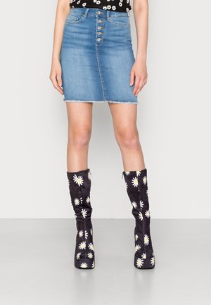 Falda de vaquera en azul claro con un dobladillo deshilachado y cinco botones plateados. Combinada con botas altas oscuras que tienen un patrón de margaritas blancas.