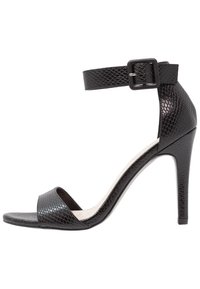 Sandales à talons hauts noires avec une texture brillante imitant le serpent, présentant une large bride avant et une bride de cheville réglable avec une boucle.