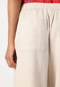Light beige linen shorts with an elastic waistband, featuring a square back pocket. The fabric has a textured, slightly coarse finish.
