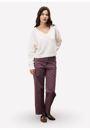 Ivory gebreide trui met V-hals, gecombineerd met hoog-waisted paarse denim broek. Model draagt bruine platte schoenen. Eenvoudige achtergrond.