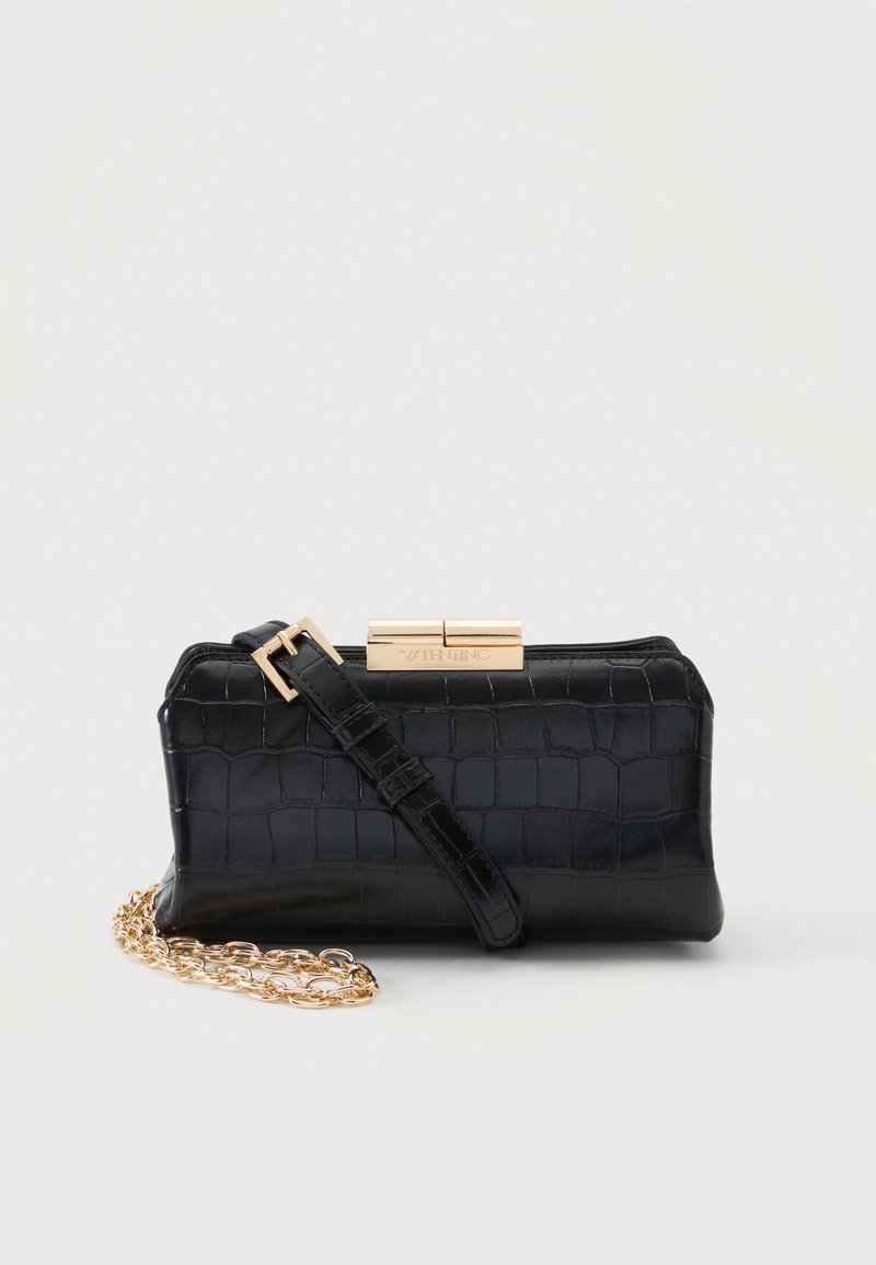 Μαύρο clutch με υφή κροκόδειλου, χρυσό κούμπωμα, ρυθμιζόμενο λουράκι και λεπτομέρεια με χρυσή αλυσίδα, τοποθετημένο σε απλό ανοιχτό φόντο.