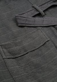 Mörkgrått tyg med ett strukturerat zigzag-mönster. Inkluderar ett knytband och en lapplomme. Mjukt och flexibelt material med en subtil lyster.