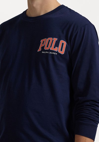 Jūrinės mėlynos ilgų rankovių marškinėliai iš medvilnės, ant krūtinės rašoma "POLO" ir "RALPH LAUREN" raudonos ir baltos spalvos tekstu, apvalus kaklas.