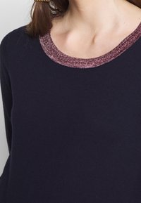 Maglione blu navy con un collo testurizzato in metallico bordeaux. Tessuto liscio, design con scollo rotondo e maniche lunghe visibili.