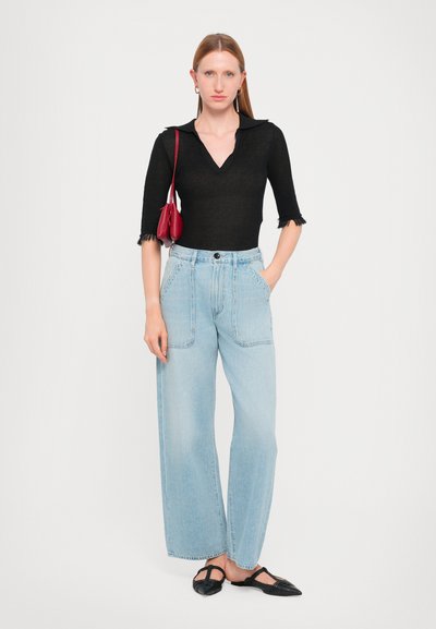 Black knit top with a collar and frayed sleeves, light blue wide-leg jeans, black flat shoes, and a small red handbag.