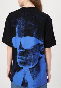 Svart oversized t-skjorte med blå grafisk portrett med solbriller, laget av myk bomull, med rund hals og korte ermer.