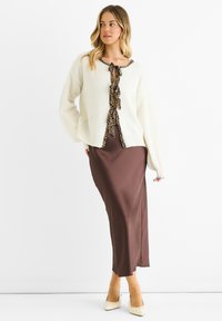 Cardigan lavorato a maglia crema con accenti in stampa leopardata, abbinato a una gonna lunga in satin marrone. L'outfit presenta una vestibilità rilassata e fiocchi alla chiusura.