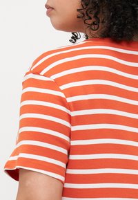 Striped shirt featuring orange and white horizontal stripes, short sleeves, ribbed neckline, and soft cotton material.