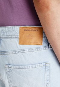 Light blue denim jeans with a brown leather label featuring “JACK & JONES” and additional text. Standard back pocket visible.