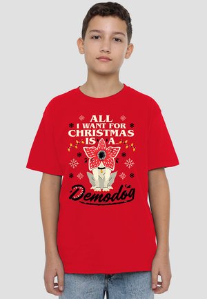 Red cotton t-shirt featuring a graphic design of a dog with a flower, snowflakes, and the text "ALL I WANT FOR CHRISTMAS IS A Demodóg."