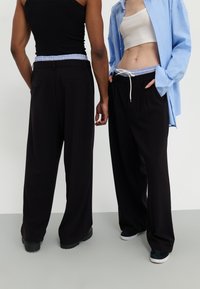 Pantalons larges noirs avec taille élastique présentant des accents bleu clair. Tissu lisse, coupe décontractée, poches avant, à associer avec divers tops.