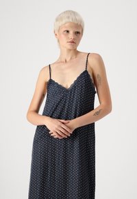 Sleeveless nightgown in navy with small, white and red polka dots. Features scalloped lace trim at the neckline. Smooth fabric texture.