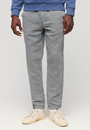 Pantalons gris texturé à coupe droite avec un motif subtil. Associés à des baskets crème et un sweat-shirt bleu.