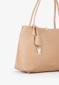 Borsa a mano in pelle beige con superficie testurizzata, hardware dorato e un charm a forma di chiave. Presenta due manici per la spalla e una forma arrotondata.