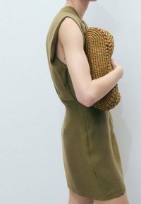 Robe sans manches vert olive avec une taille cintrée et une texture lisse, accompagnée d'un sac à main tressé couleur beige au design arrondi.