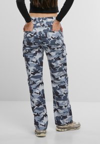 Pantalones cargo de camuflaje azul y gris con bolsillos, de corte holgado y cintura a media altura, combinados con zapatillas beige.