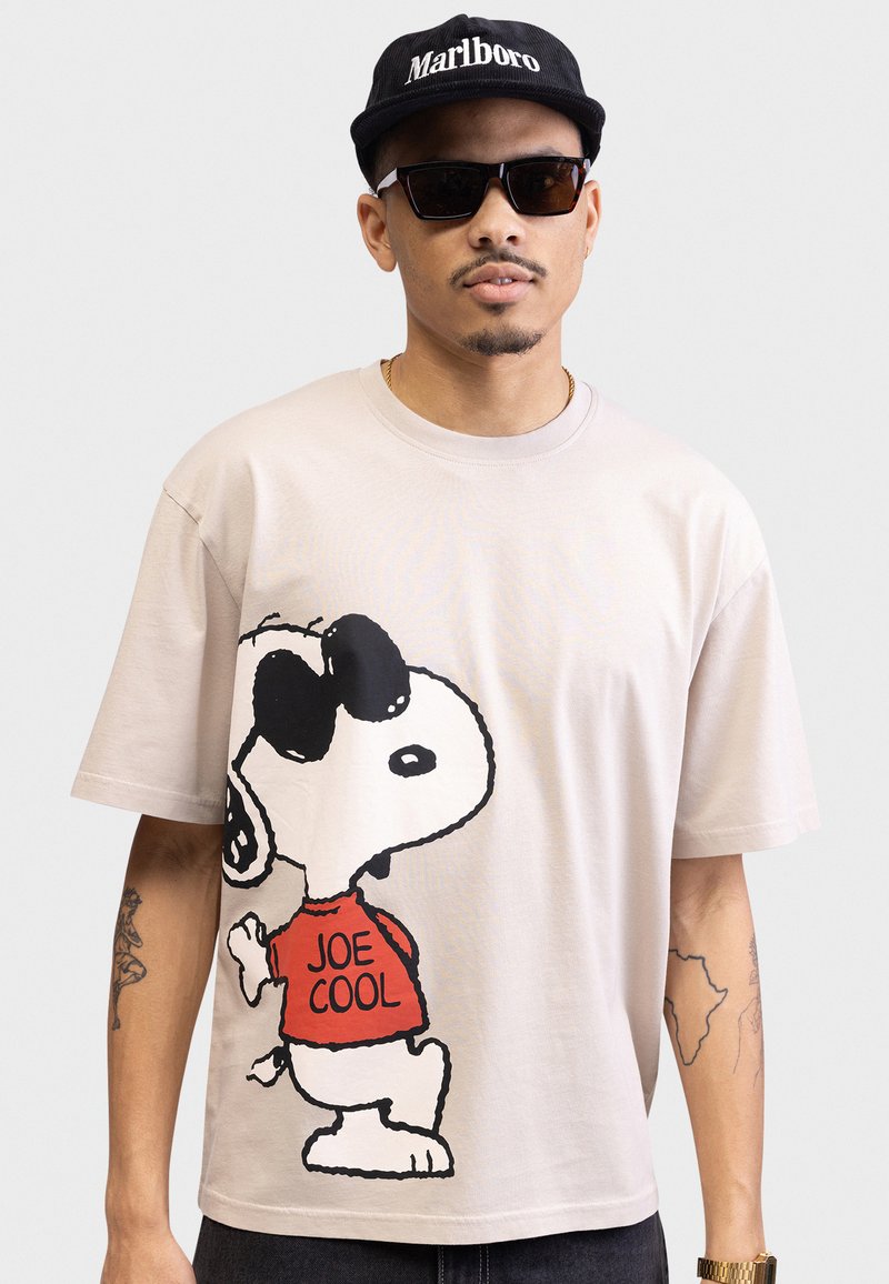 Heledad beež puuvillane T-särk, millel on suur graafika Snoopy'st, kes kannab prille ja punast "JOE COOL" särk. Lühikesed varrukad ja lõdva lõikega.