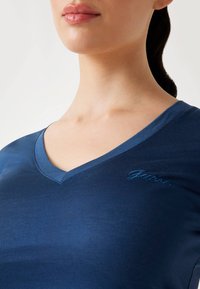 Námornícky modré tričko s výstrihom do V, vyrobené z mäkkej tkaniny, s jemne vyšitým logom na ľavej strane. Hladká textúra a priliehavý strih.