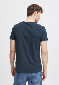 Camiseta de manga corta azul oscuro hecha de una tela suave, con un cuello redondo y un corte recto, vista desde atrás.