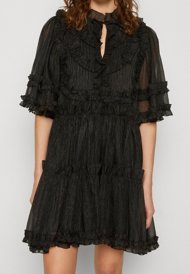 Robe courte noire transparente avec des volants en couches aux manches, au corsage, à la taille et à l'ourlet, avec un petit keyhole au niveau du col et un tissu texturé.
