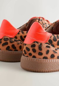 Leopardenmuster-Sneaker mit einem Obermaterial aus braunem Kunstfell, leuchtend orangefarbenem Lederakzent an der Ferse und einer strukturierten Gummisohle.