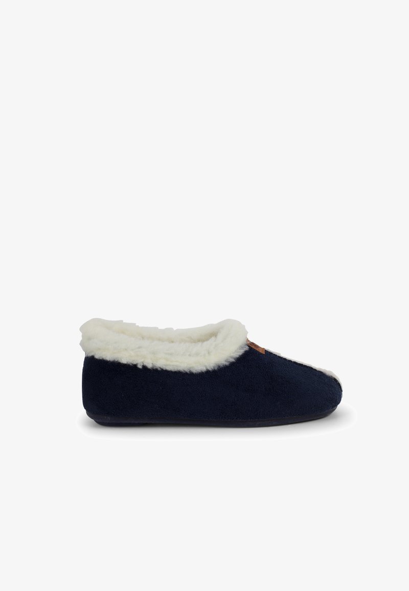Granatowe kapcie z miękkim, białym futerkiem, zaokrąglonym czubkiem i teksturowanym wykończeniem, z małym brązowym logo akcentowym.