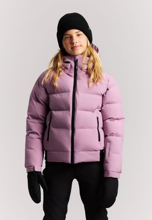 Young person wearing a pink puffer jacket, black winter hat, black mittens, and black pants, standing against a plain background.